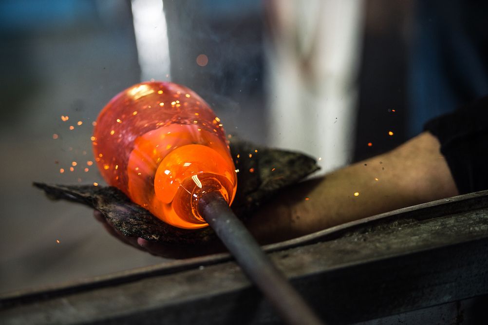 person shaping hand blown glass in a hot shop