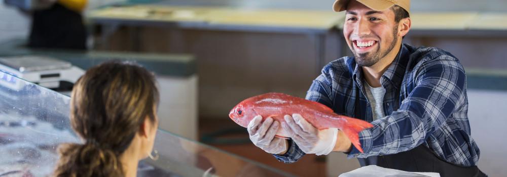 fishmonger handing a woman a fresh fish